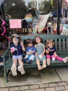 a group of four young children enjoying some ice cream on a bench in front of the Gem Mountain store front