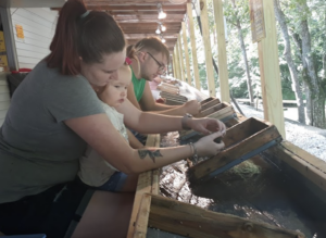 families, including a mother and young child, sift through earth and sand looking for gemstones at Gem Mountain