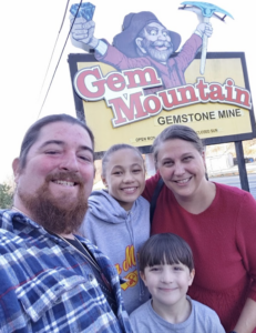 A family poses for a picture in front of the Gem Mountain sign